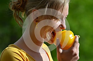 Blond girl eating yellow pepper