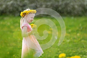 Blond girl in field of yellow dandelions. Summer day. Little lady in pink dress holds flowers. Selective focus