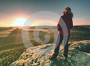 Blond girl with hands in jacket pockets hiking in mountains