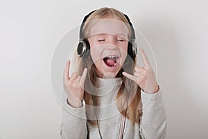 Blond girl with headphones listening music and singing. Cute little girl making a rock-n-roll sign.