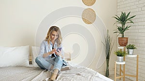 Blond girl in jeans sits on bed working on smartphone