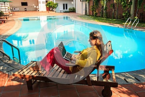 Blond Girl Lies on Chaise-longue with Laptop at Pool in City