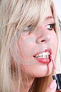 Blond girl making up her lips with a lipgloss