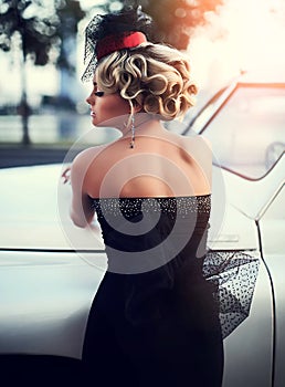 Blond girl model with bright makeup and curly hairstyle in retro style posing near old white car