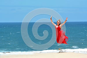 Blond girl with red dress jumping on beach