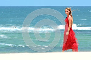 Blond girl with red dress walking on beach