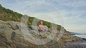 Blond girl relaxes in yoga pose on large high rock