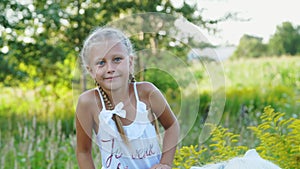Blond girl of seven years, in a white dress, climbs, sits on a pony. Cheerful, happy family vacation. Outdoors, in the