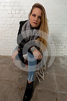 Blond girl sitting green eyes white brick wall