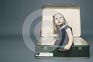 Blond girl sitting in a vintage suitcase