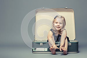 Blond girl sitting in a vintage suitcase