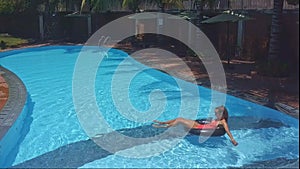 Blond girl swims on inflatable ring in pool