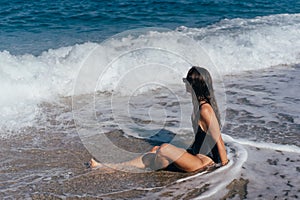 Blond girl in swimsuit sitting at sea beach tanning