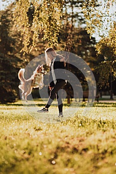 Blond girl train her dog border collie in green park in sunshine