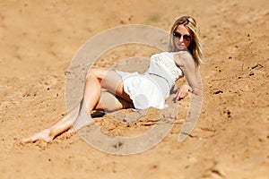Blond girl in white dress relaxing on sand
