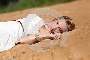 Blond girl in white dress relaxing on sand
