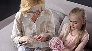 Blond grandmother knitting with her little granddaughter at home, handmade