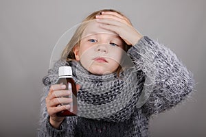 Blond hair little girl holding cough syrup in a hand. Sick child.. Child winter flu health care concept