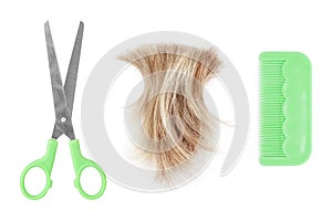 Blond hair lock, metal scissors, green plastic comb white background isolated close up, cut off blonde hair curl, shears, brush