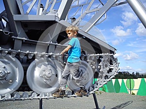 A blond-haired boy in a blue T-shirt climbed onto a metal structure. An old tractor with caterpillar wheels turned into a mosquito