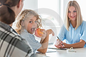 Blond haired boy eating an apple while visiting a dietitian