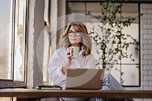 Blond haired entrepreneur sitting at desk with her computer and looking thoughtfully