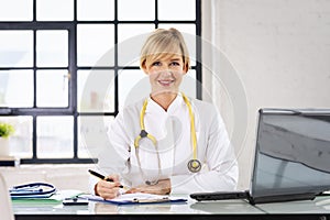 Blond haired female doctor sitting at desk and making notes