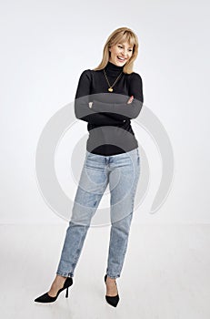 Blond haired woman wearing black sweater and blue jeans and standing against isolated background