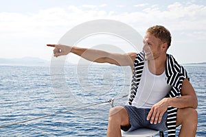 Blond handsome young man on a sailing boat pointing at something