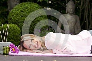 Blond happy middle aged woman lying on a blanket in zen garden