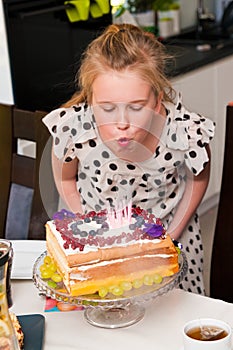 Blond happy young girl blowing candles on her birthday cake