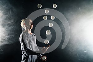 Blond juggler with white balls on black background