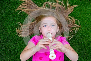 Blond kid children girl playing flute lying on grass