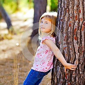 Blond kid girl on autumn tree trunk