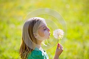 Blond kid girl blowing dandelion flower in green meadow