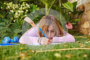 Blond kid girl homework lying on grass turf