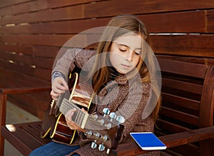 Blond kid girl learning play guitar with smartphone