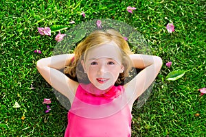 Blond kid girl lying on garden grass smiling aerial view