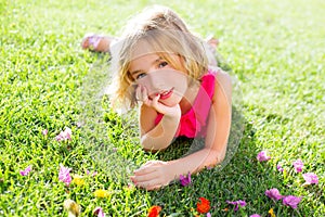 Blond kid girl lying relaxed in garden grass with flowers