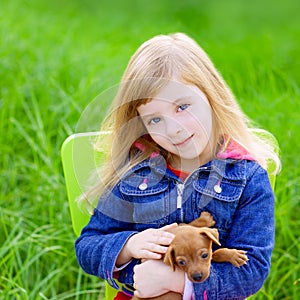 Blond kid girl with puppy pet dog in green grass