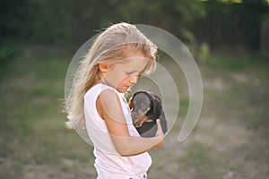 Blond kid girl with puppy pet dog in hands outdoors. Side view