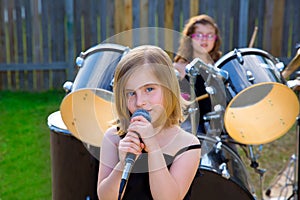Blond kid girl singing in tha backyard with drums
