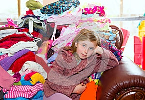 Blond kid girl sitting on a messy clothes sofa