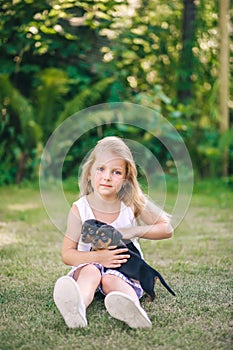 Blond kid girl in white dress with puppy pet dog sit in outdoor green grass