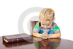 Blond little boy praying to God after reading the bible
