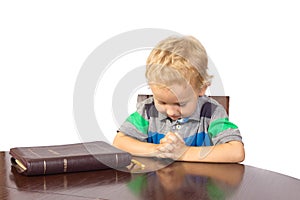 Blond little boy praying to God after reading the bible