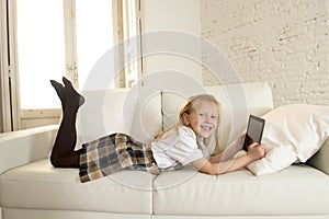 Blond little girl lying on home sofa couch using internet app on digital tablet pad on digital tablet pad