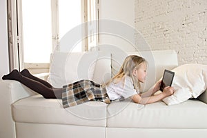 Blond little girl lying on home sofa couch using internet app on digital tablet pad on digital tablet pad photo