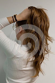 Blond long natural hair being styled into ponytail by young caucasian woman wearing white outfit and gold glasses