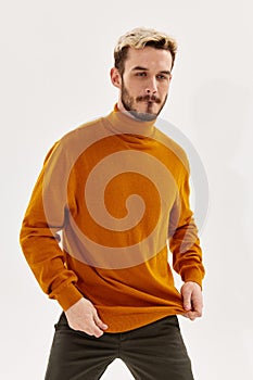 blond man in an orange sweater on a light background and dark trousers cropped view